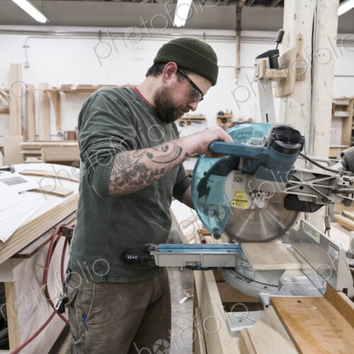 Caucasian male carpenter using a radial saw to cut a piece of wood in a large… Caucasian male carpenter using a radial saw to cut a piece of wood in a large…
