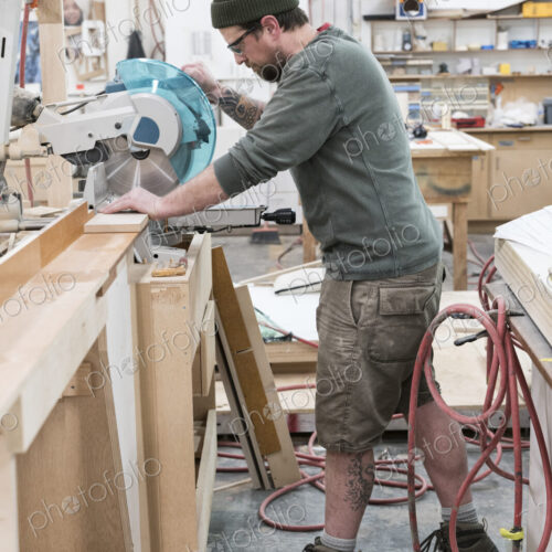 Caucasian male carpenter using a radial saw to cut a piece of wood in a large… Caucasian male carpenter using a radial saw to cut a piece of wood in a large…