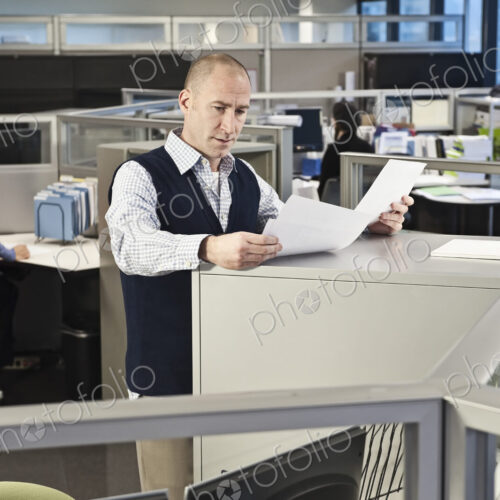 Caucasian male going over paperwork in office cubicles. Caucasian male going over paperwork in office cubicles.