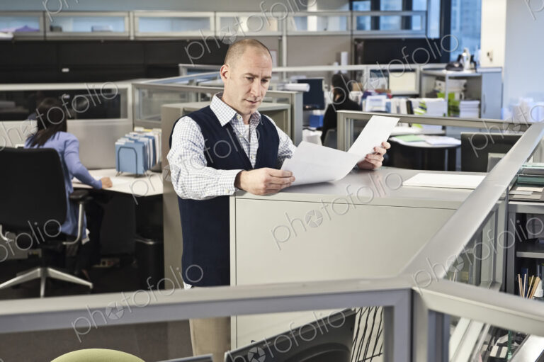 Caucasian male going over paperwork in office cubicles.