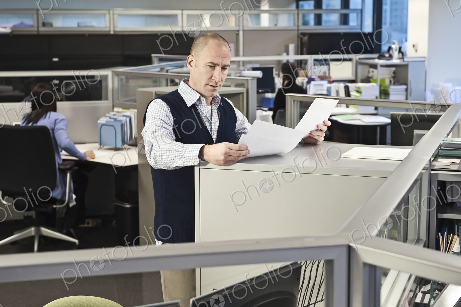 Caucasian male going over paperwork in office cubicles.