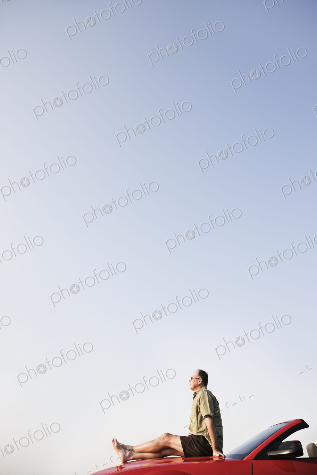 Caucasian male relaxing on the hood of his convertible sports car.