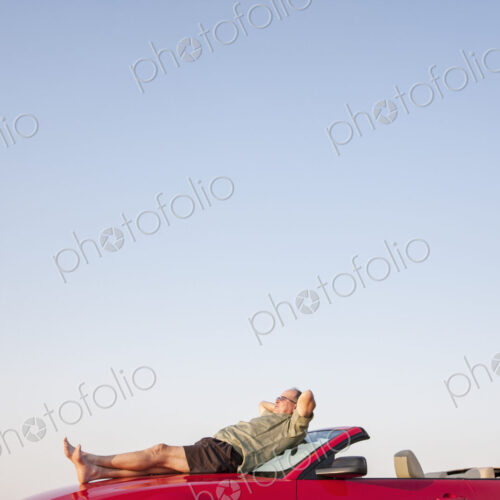 Caucasian male relaxing on the hood of his convertible sports car. Caucasian male relaxing on the hood of his convertible sports car.