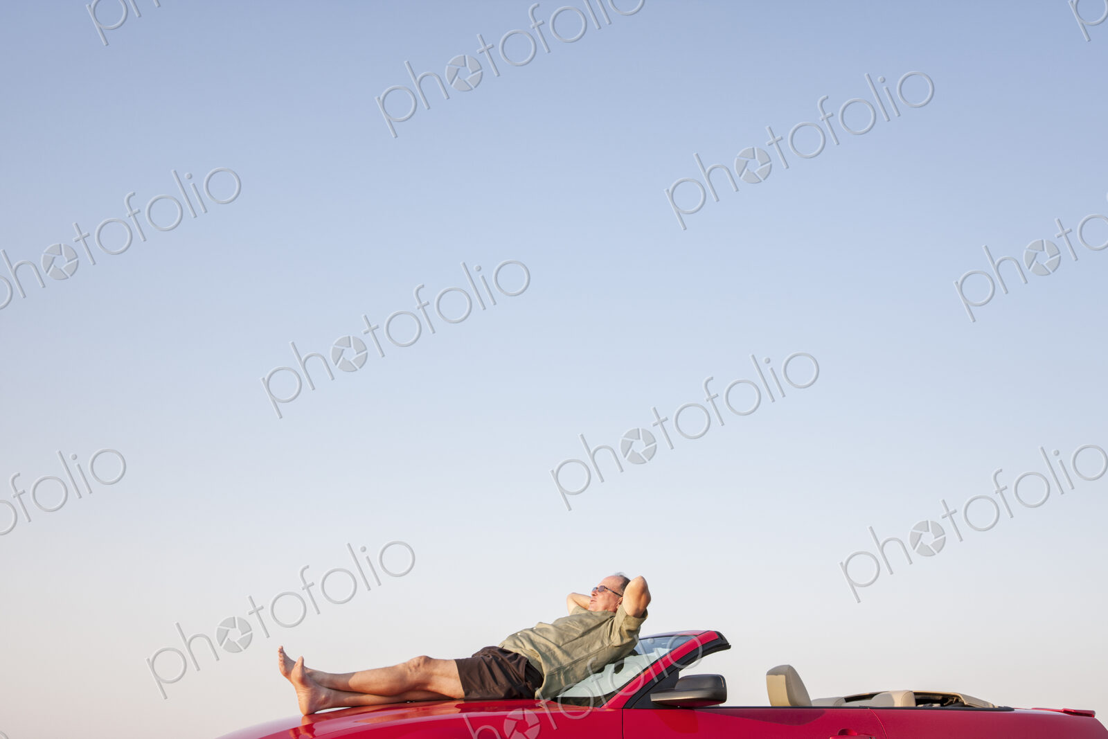 Caucasian male relaxing on the hood of his convertible sports car.
