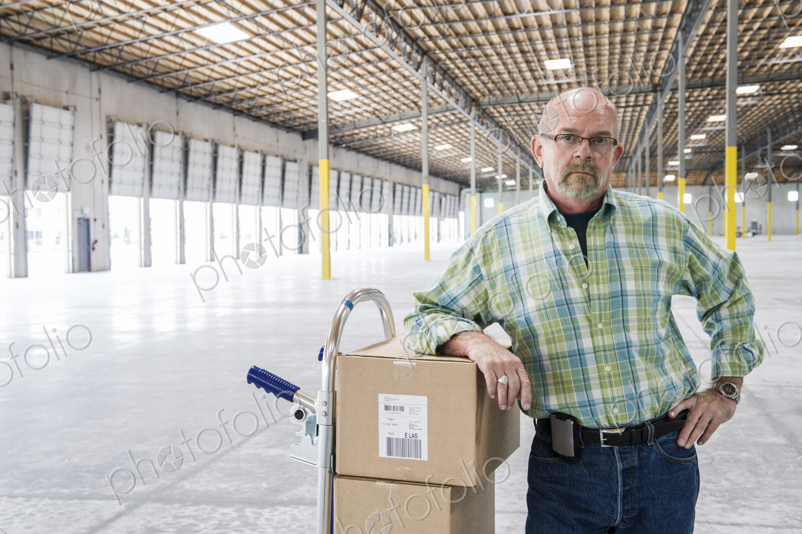 Caucasian male standing next to hand truck in front of loading dock doors inside of a…