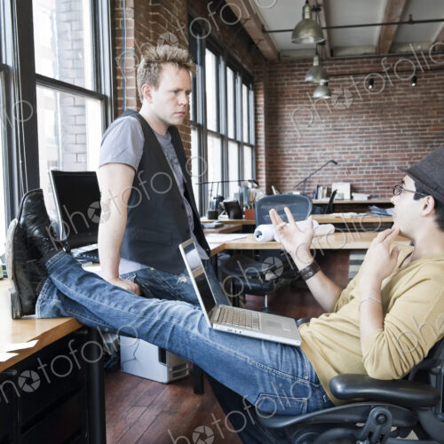 Caucasian man and Hispanic man discussing a problem at a creative office work station.