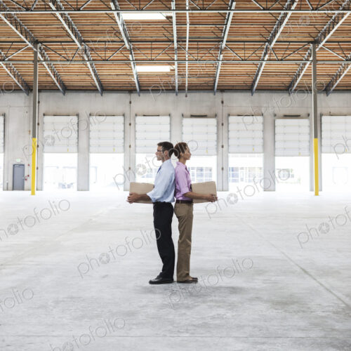 Caucasian man and black female holding cardboard boxes in middle of empty warehouse… Caucasian man and black female holding cardboard boxes in middle of empty warehouse…