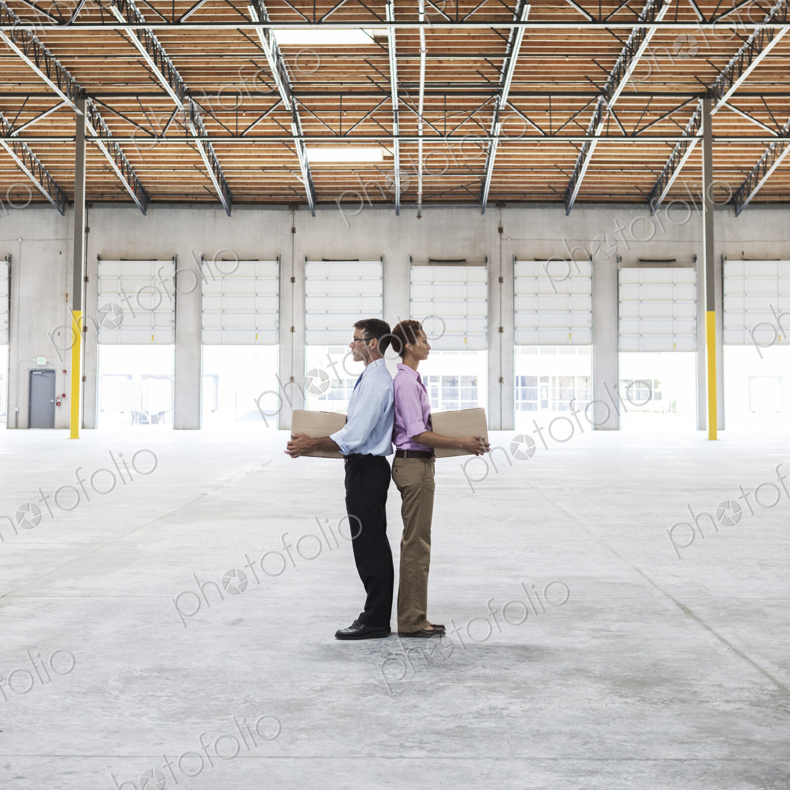 Caucasian man and black female holding cardboard boxes in middle of empty warehouse…