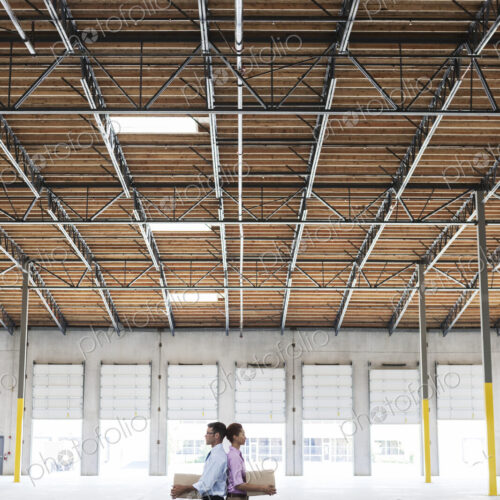 Caucasian man and black female holding cardboard boxes in middle of empty warehouse… Caucasian man and black female holding cardboard boxes in middle of empty warehouse…