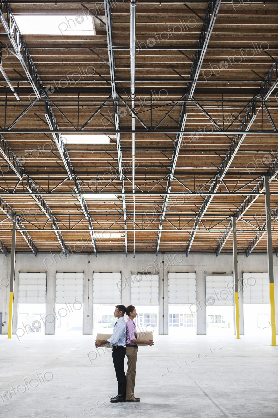 Caucasian man and black female holding cardboard boxes in middle of empty warehouse…