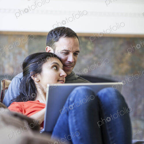 Caucasian man and mixed race caucasian woman using a lap top computer while sitting on… Caucasian man and mixed race caucasian woman using a lap top computer while sitting on…