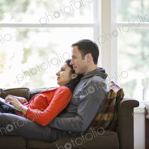 Caucasian man and mixed race caucasian woman using a laptop computer while sitting on… Caucasian man and mixed race caucasian woman using a laptop computer while sitting on…