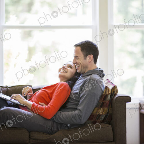 Caucasian man and mixed race caucasian woman using a laptop computer while sitting on… Caucasian man and mixed race caucasian woman using a laptop computer while sitting on…
