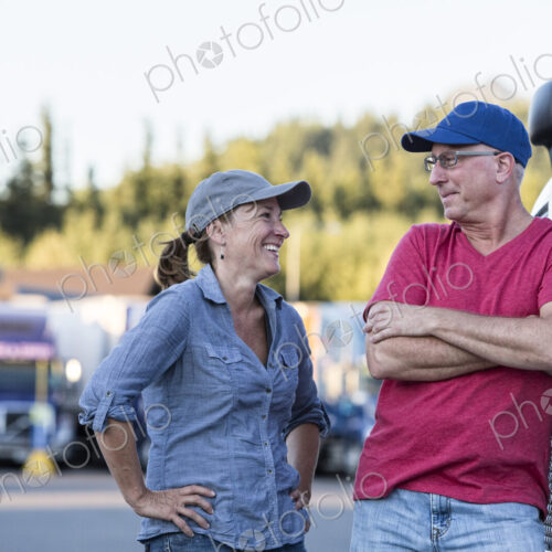 Caucasian man and woman driving team talking in front of a large truck at a truck stop. Caucasian man and woman driving team talking in front of a large truck at a truck stop.