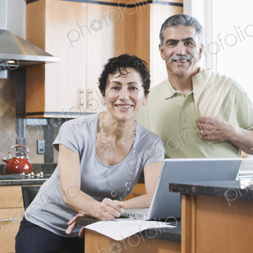Caucasian man and woman in a kitchen using a laptop. Caucasian man and woman in a kitchen using a laptop.