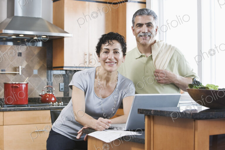 Caucasian man and woman in a kitchen using a laptop.