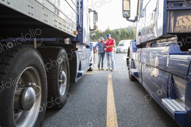 Caucasian man and woman truck driving team going over data on a cell phone while…