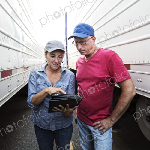 Caucasian man and woman truck driving team going over data on a cell phone while… Caucasian man and woman truck driving team going over data on a cell phone while…