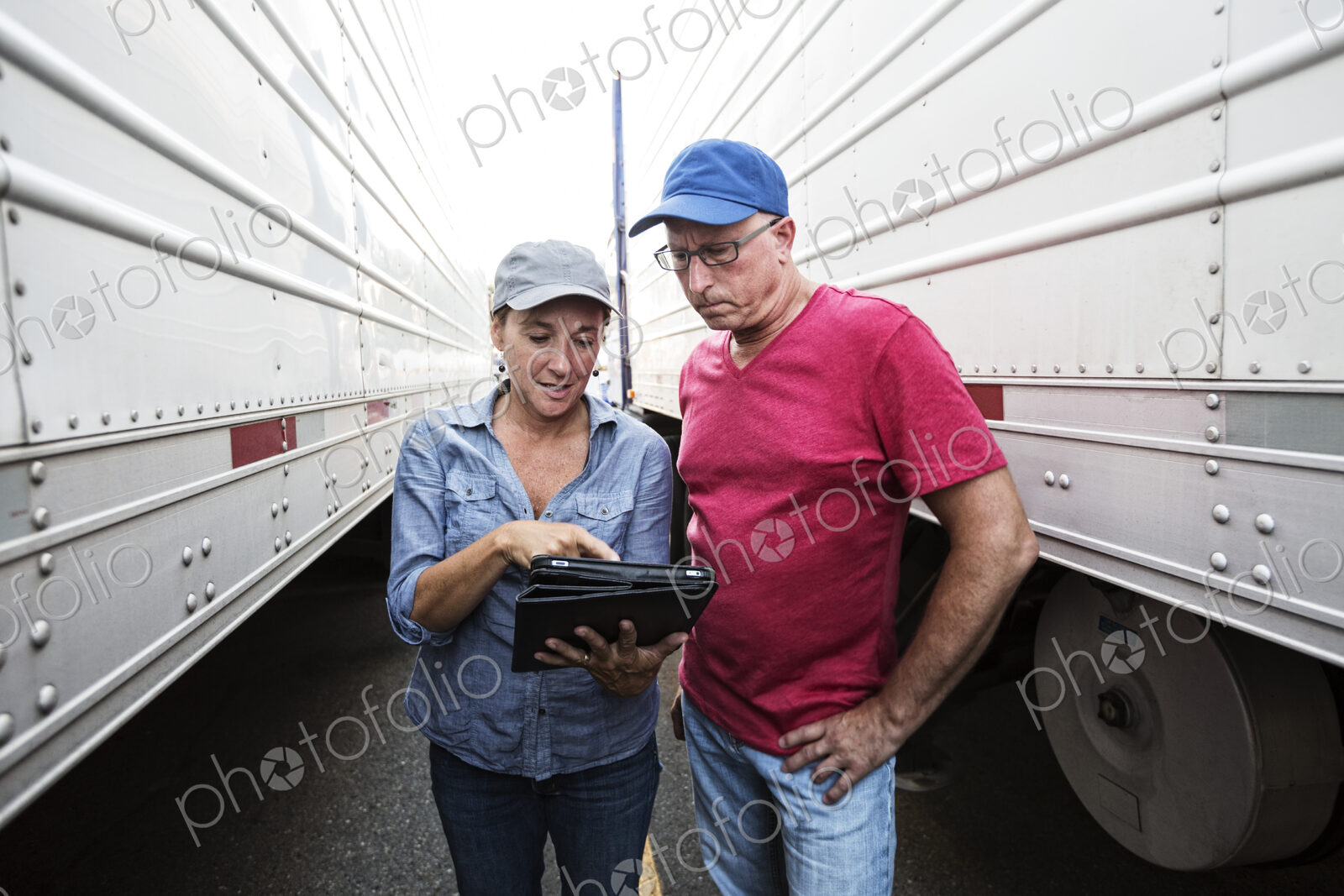 Caucasian man and woman truck driving team going over data on a cell phone while…