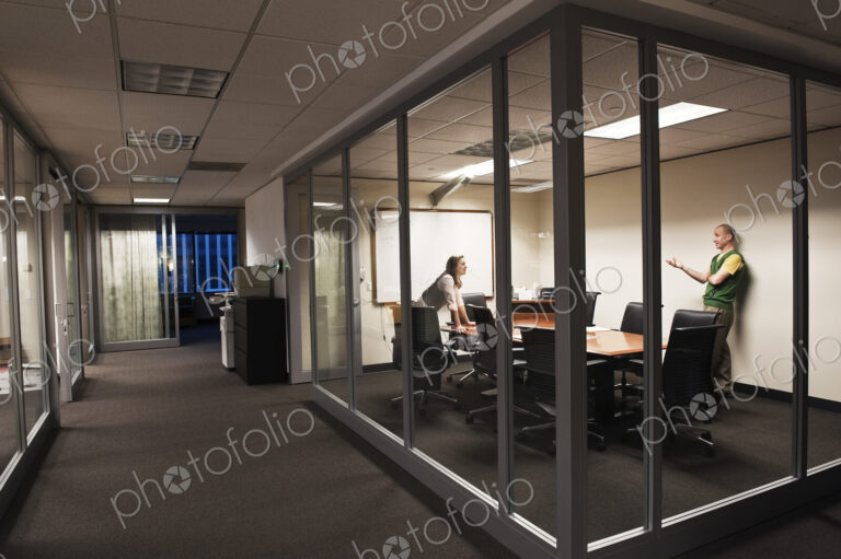 Caucasian man and woman working after hours in an office conference room.