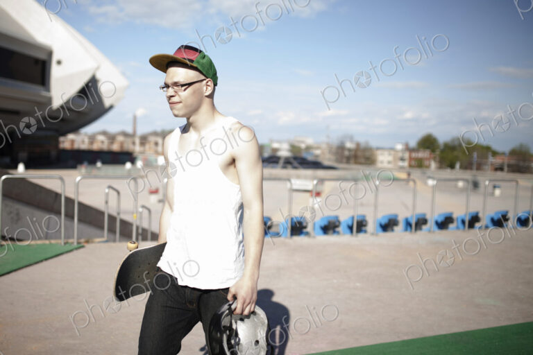 Caucasian man carrying skateboard near stadium