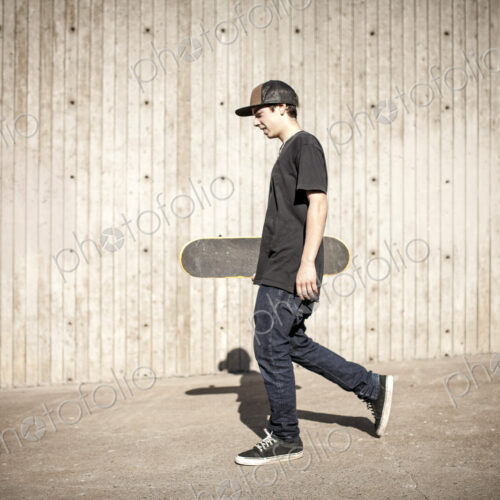 Caucasian man carrying skateboard near wooden wall