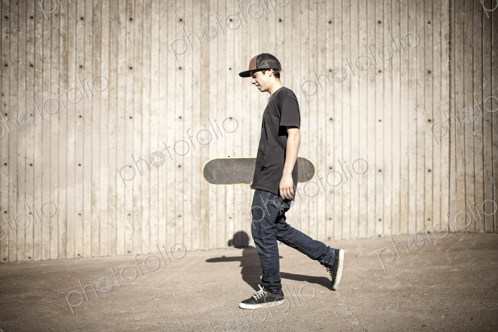 Caucasian man carrying skateboard near wooden wall