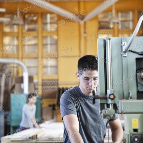 Caucasian man cutting wood using a band saw in a woodworking factory.