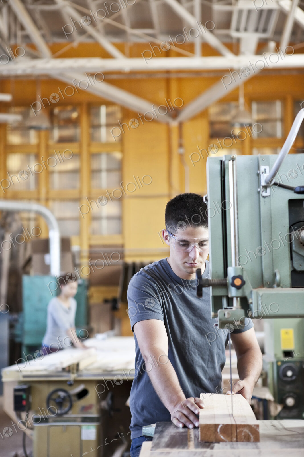 Caucasian man cutting wood using a band saw in a woodworking factory.