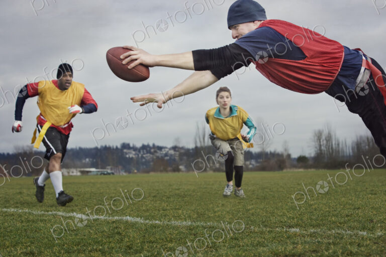 Caucasian man diving over the score line holding a football during an non-contact flag…
