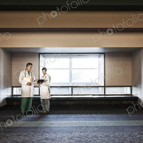 Caucasian man doctor and asian woman doctor conferring in hospital hallway. Caucasian man doctor and asian woman doctor conferring in hospital hallway.