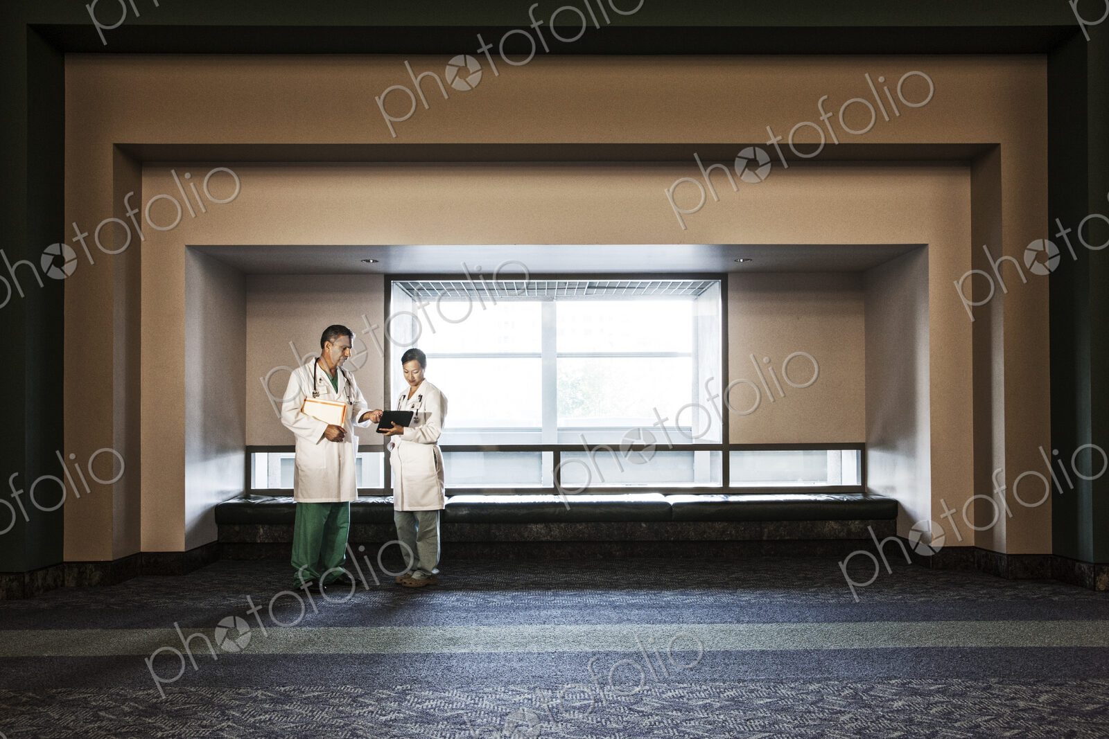 Caucasian man doctor and asian woman doctor conferring in hospital hallway.