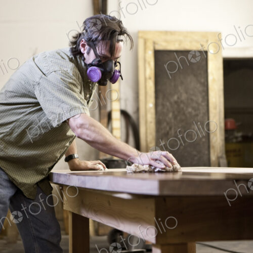 Caucasian man factory worker applying finish stain to the top of a table in a…