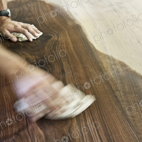 Caucasian man factory worker applying finish to a recycled wood table top in a…