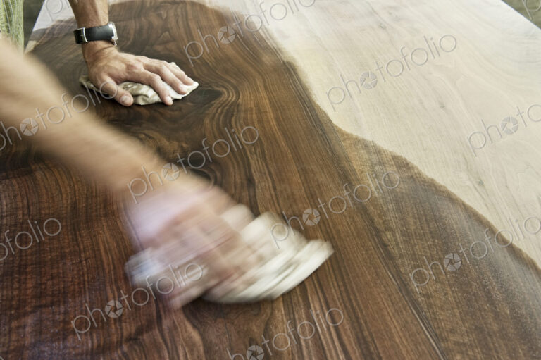 Caucasian man factory worker applying finish to a recycled wood table top in a…