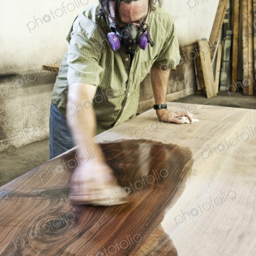 Caucasian man factory worker applying finish to a recylced wood table top in a…
