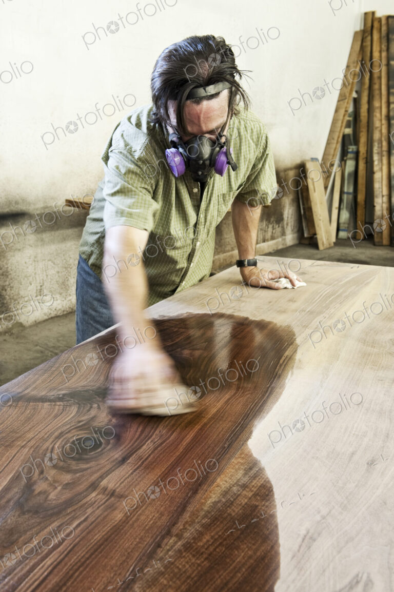 Caucasian man factory worker applying finish to a recylced wood table top in a…