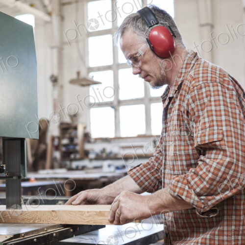Caucasian man factory worker cutting wood using a band saw in a woodworking factory. Caucasian man factory worker cutting wood using a band saw in a woodworking factory.