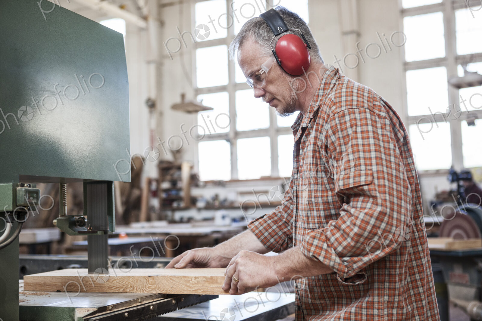 Caucasian man factory worker cutting wood using a band saw in a woodworking factory.