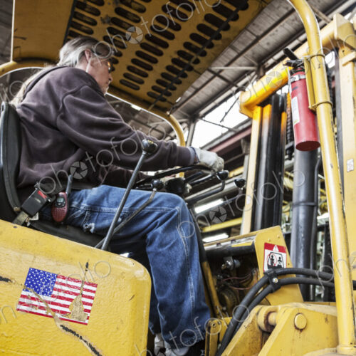 Caucasian man factory worker driving a fork lift in a sheet metal factory. Caucasian man factory worker driving a fork lift in a sheet metal factory.