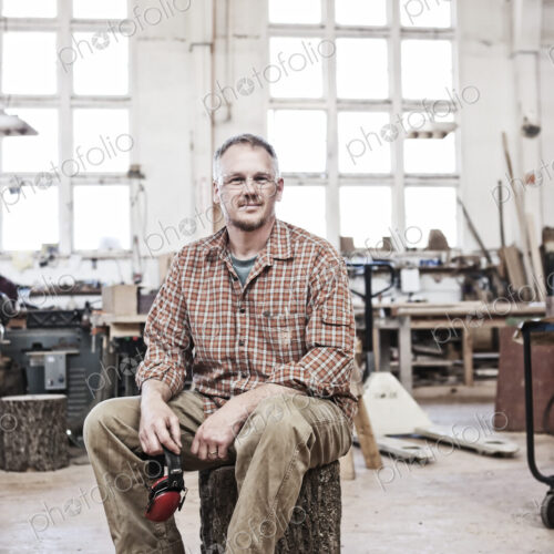 Caucasian man factory worker sitting on a stool in a woodworking factory. Caucasian man factory worker sitting on a stool in a woodworking factory.