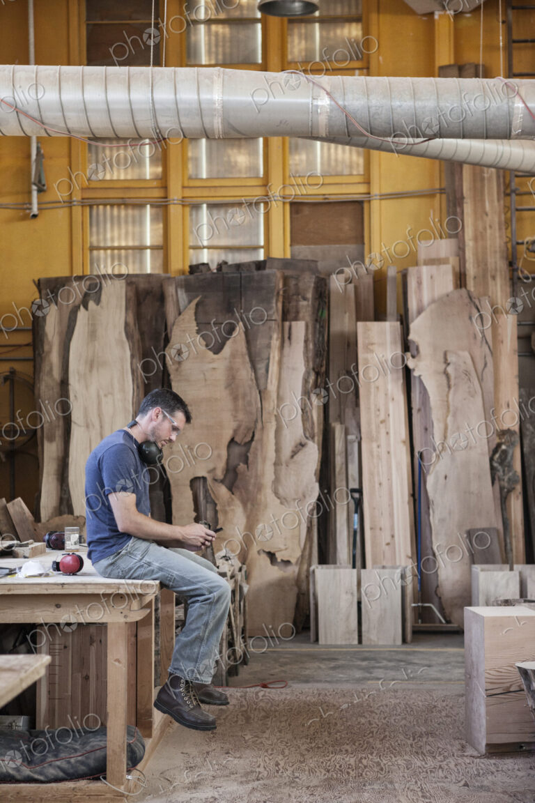 Caucasian man factory worker taking a break checking phone messages in a woodworking…