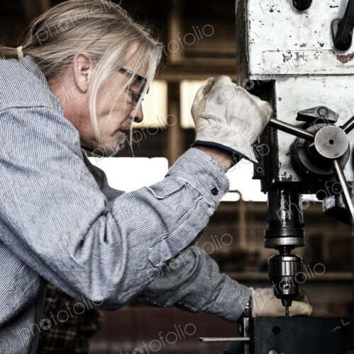 Caucasian man factory worker using a drill press in a sheet metal factory.