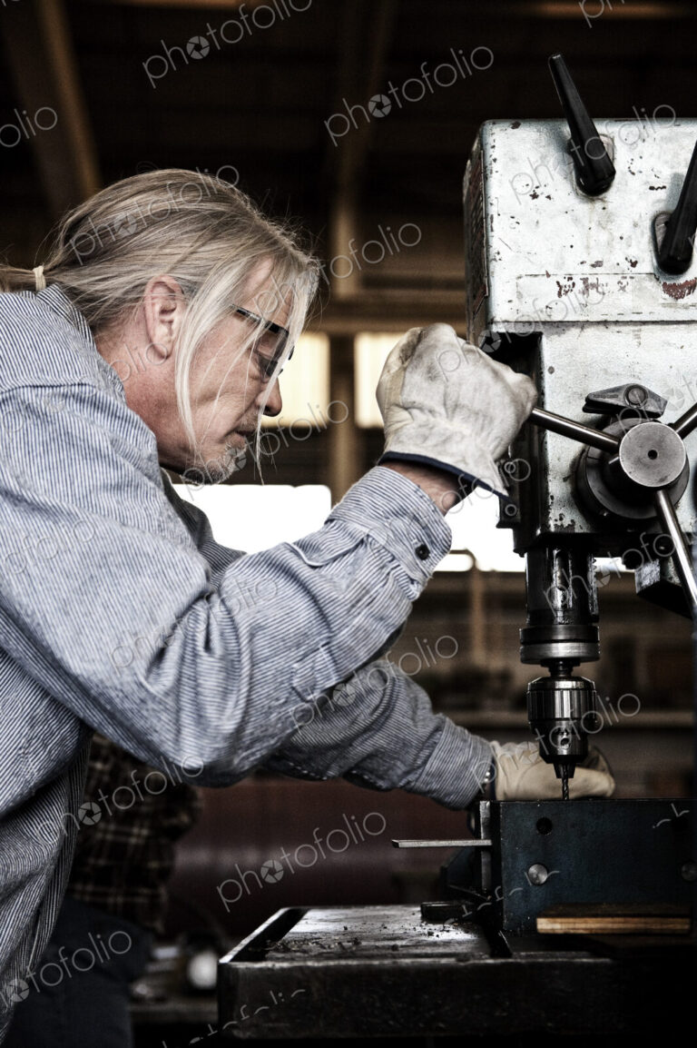 Caucasian man factory worker using a drill press in a sheet metal factory.
