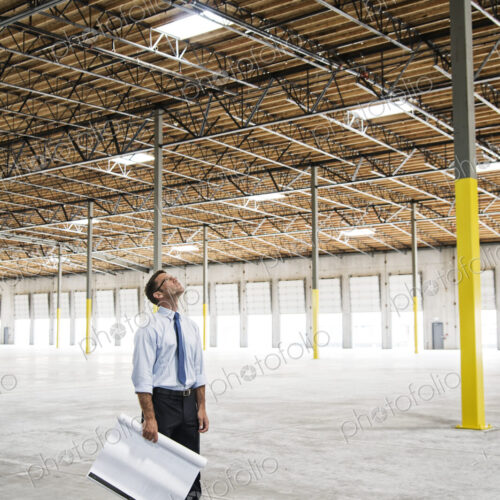 Caucasian man going over plans for new warehouse interior in front of loading dock doors.