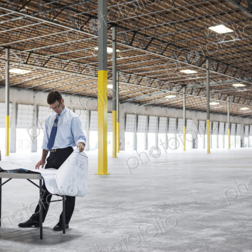 Caucasian man going over plans for new warehouse interior in front of loading dock doors.