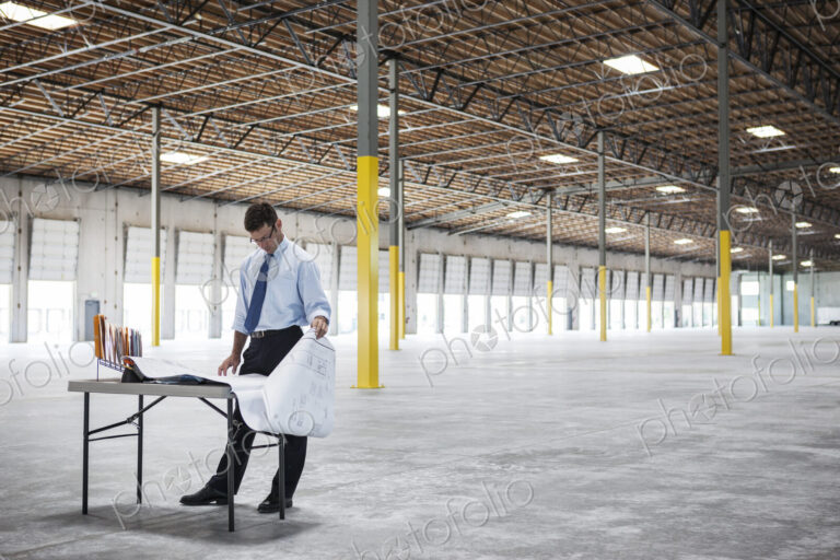 Caucasian man going over plans for new warehouse interior in front of loading dock doors.