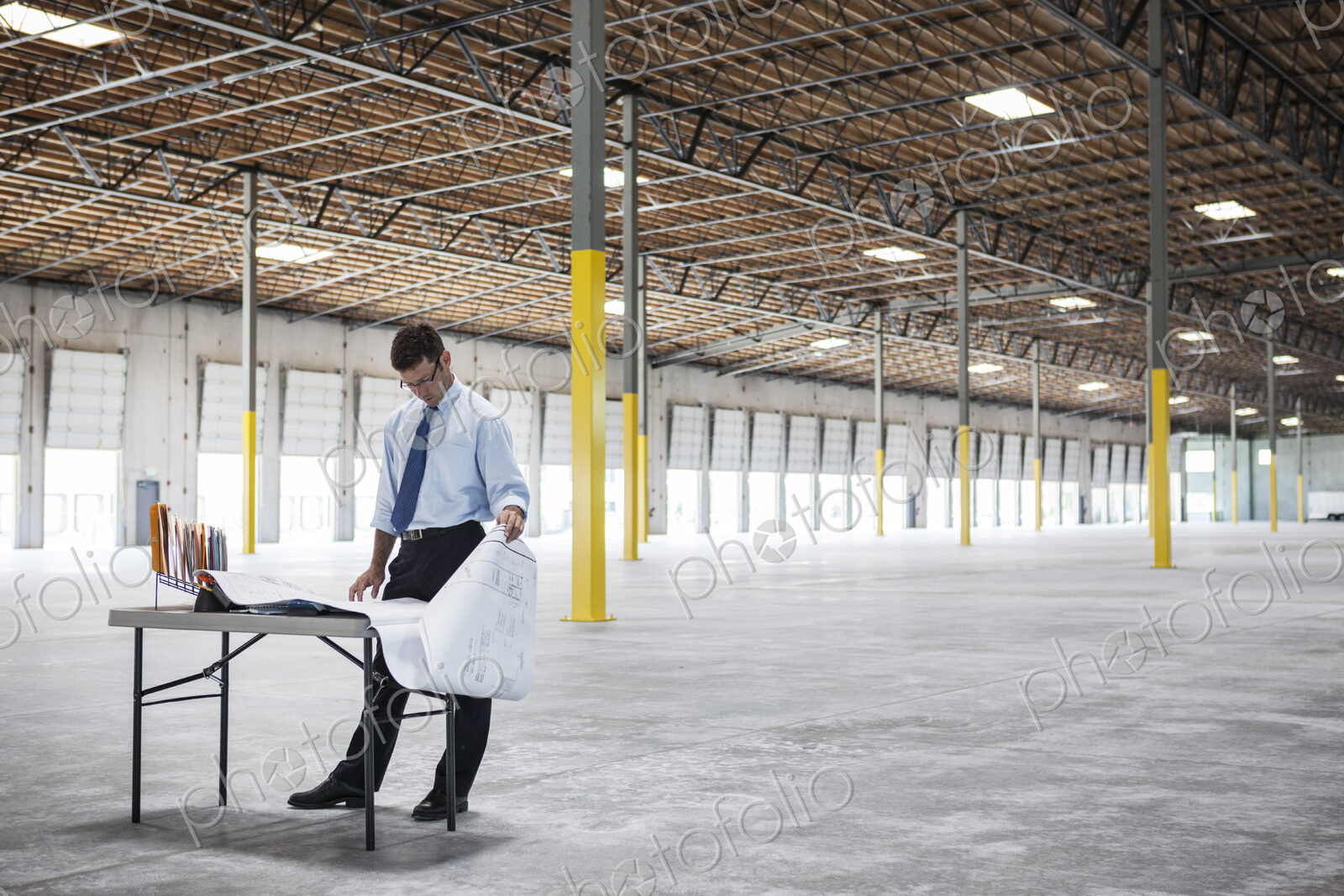 Caucasian man going over plans for new warehouse interior in front of loading dock doors.