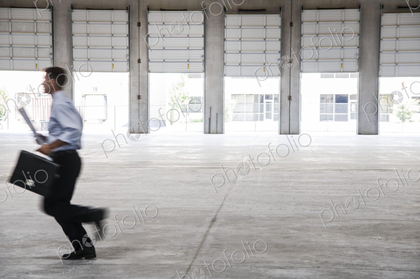 Caucasian man in dress shirt and slacks carrying brief case and plans running though…