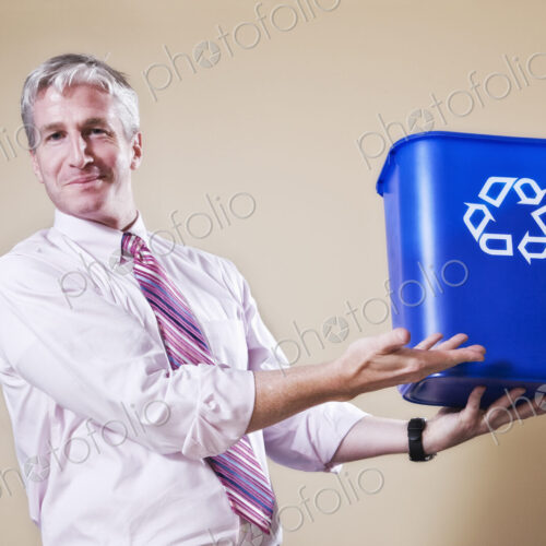 Caucasian man in shirt and tie holding a recycle waste bin.